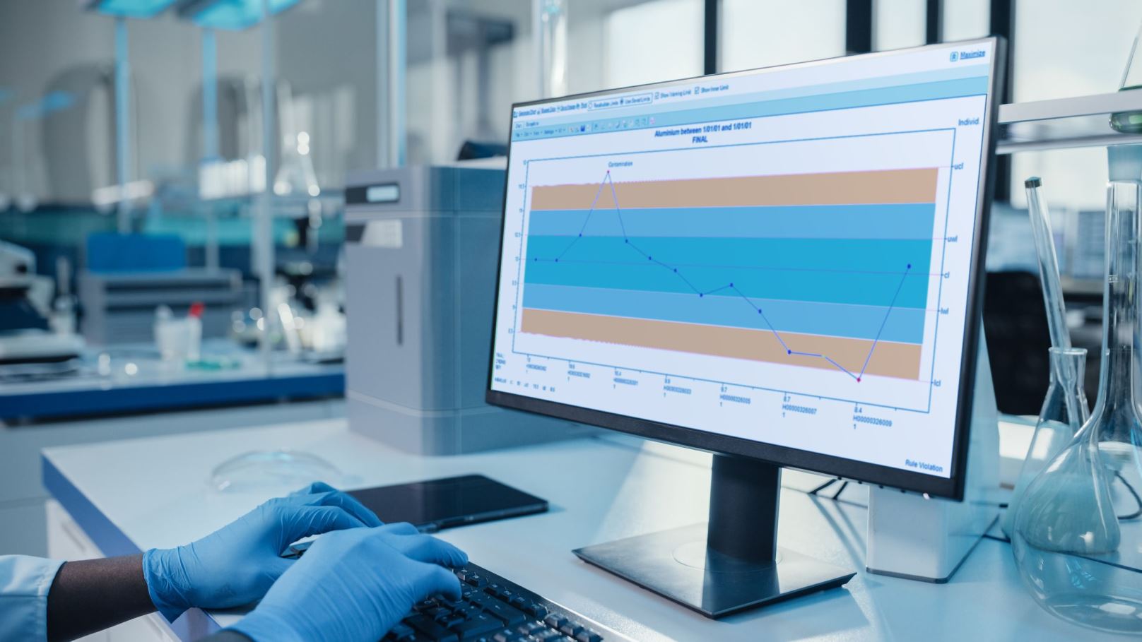 Person with gloves reviews data on their desktop computer with the STARLIMS laboratory information management system (LIMS) for R&D and Quality Manufacturing.